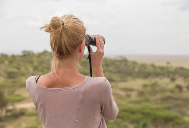 Female tourist looking through binoculars on African safari in Serengeti national park, Tanzania, Afrika.