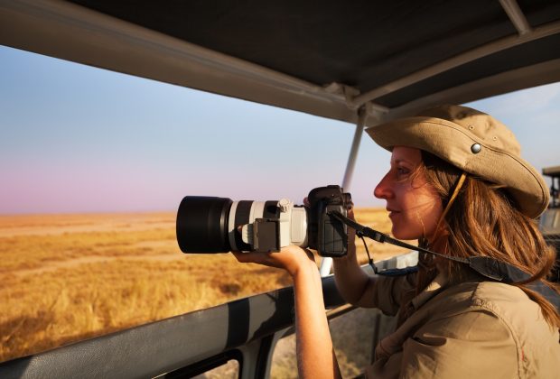 Woman taking photo with professional camera aboard safari jeep at African savannah